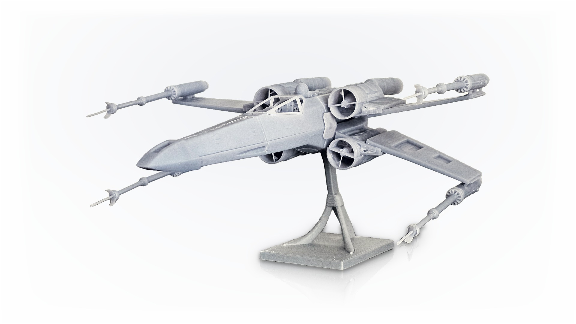 3D nyomtatott X-wing űrhajómodell állványon, fehér háttér előtt